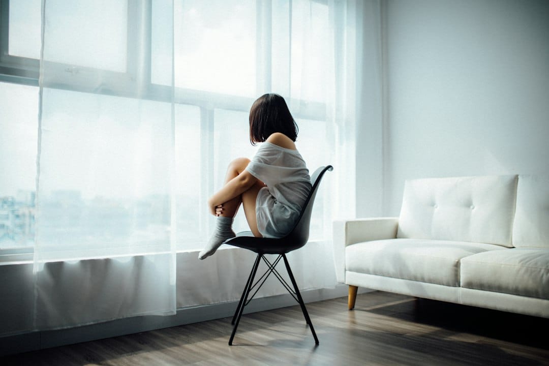 Depressed Girl Sitting on Chair Looking out of Window   Kavahana