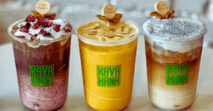 Kavahana signature kava nectar drinks live tingly >thisisjustarandomplaceholder<kavahana Three Kava Nectar Drinks from Kavahana Displayed on a Table Each Drink Shows a Different Color and Flavor Pink Topped with Rose Petals Golden Yellow and Creamy Brown with White Foam All Cups Feature the Kavahana Logo and a Wooden live Tingly Garnish